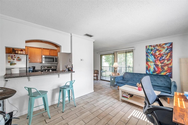 10195 Sailwinds Blvd N Unit 208, Largo, FL 33773 - kitchen featuring appliances with stainless steel finishes, crown molding, brown cabinetry, a breakfast bar area, and a textured ceiling