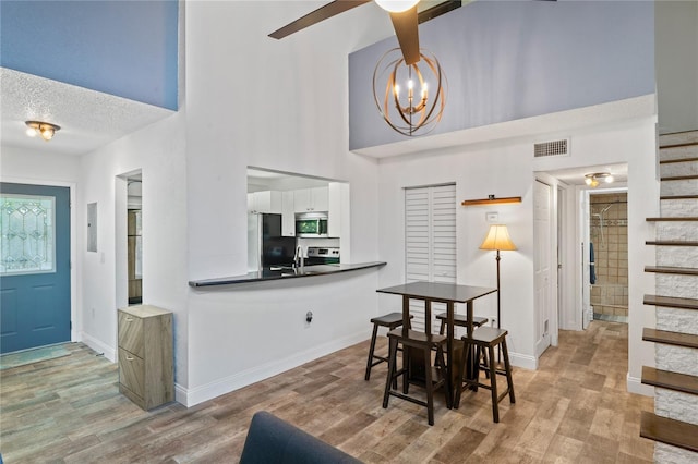 2095 Sunset Point Rd Unit 2201, Clearwater, FL 33765 - dining room featuring a chandelier, a towering ceiling, light wood finished floors, stairway, and a textured ceiling