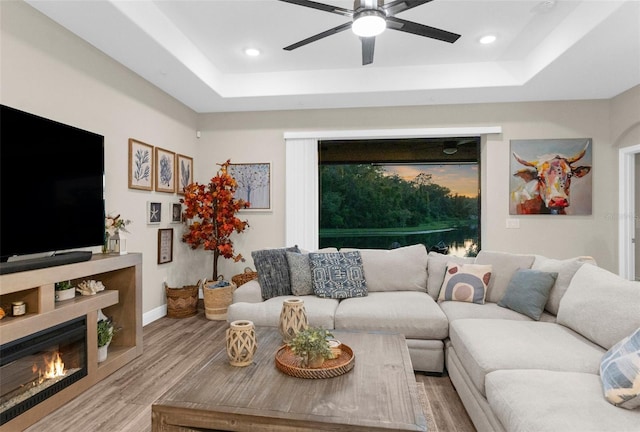 11597 Weaver Hollow Rd, New Port Richey, FL 34654 - living area with a tray ceiling, ceiling fan, light wood-style flooring, a glass covered fireplace, and recessed lighting