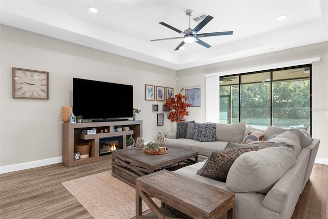 11597 Weaver Hollow Rd, New Port Richey, FL 34654 - living area with a tray ceiling, wood finished floors, ceiling fan, recessed lighting, and a glass covered fireplace