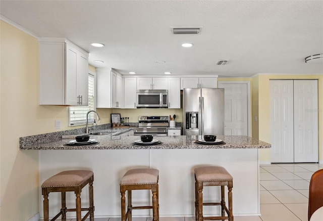 7401 Islander Ln, Hudson, FL 34667 - kitchen featuring appliances with stainless steel finishes, a peninsula, light stone counters, a kitchen bar, and white cabinets