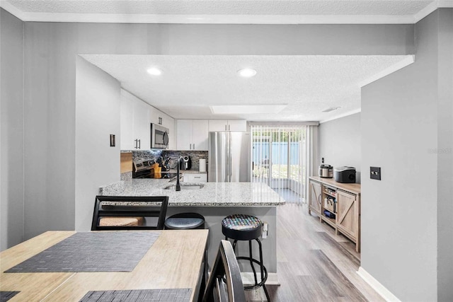 3350 Fox Hunt Dr, Palm Harbor, FL 34683 - kitchen featuring stainless steel appliances, a textured ceiling, light wood-style floors, white cabinetry, and backsplash
