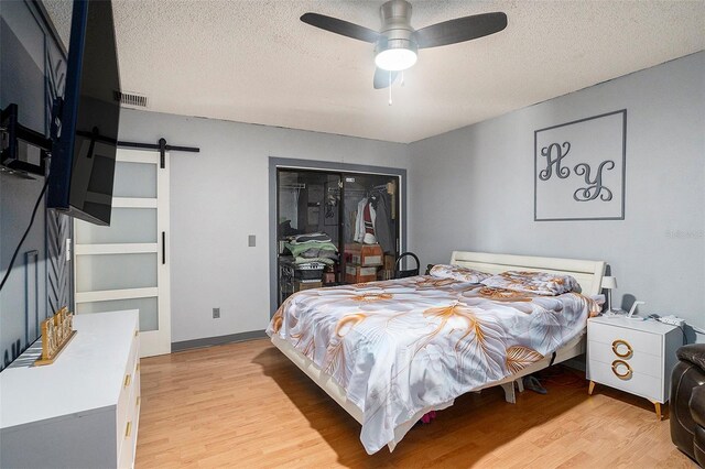 15906 Country Farm Pl, Tampa, FL 33624 - bedroom featuring light wood finished floors, a barn door, a textured ceiling, a closet, and ceiling fan