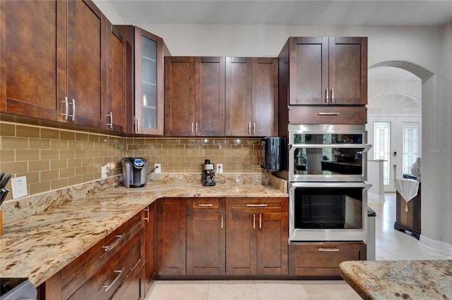 13102 Done Groven Dr, Dover, FL 33527 - kitchen featuring stainless steel double oven, decorative backsplash, light stone countertops, and glass insert cabinets