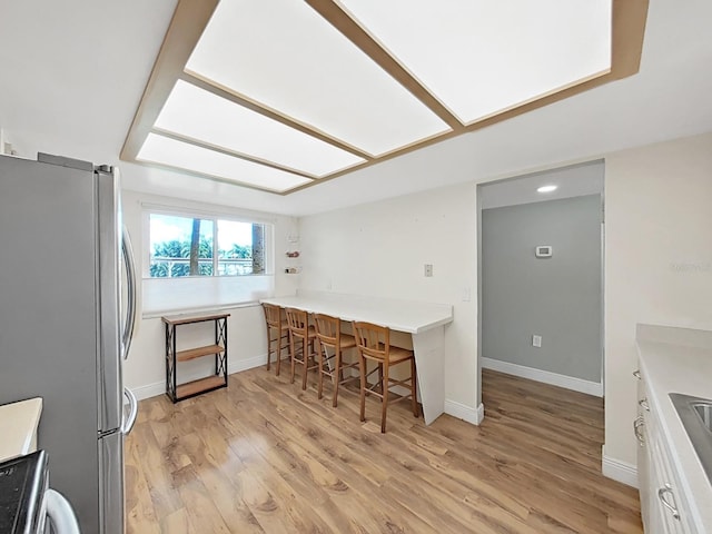 700 Starkey Rd Unit 311, Largo, FL 33771 - kitchen with freestanding refrigerator, light wood-type flooring, range, a breakfast bar area, and white cabinetry