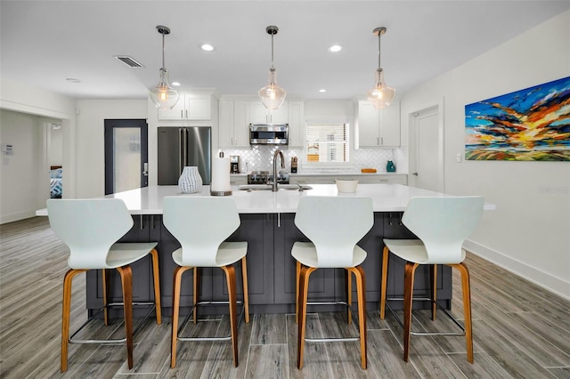 4381 Poinsettia Dr, St Pete Beach, FL 33706 - kitchen with appliances with stainless steel finishes, light wood-type flooring, tasteful backsplash, white cabinets, and a large island