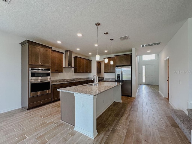 38120 Shale Stone Ct, Zephyrhills, FL 33540 - kitchen with appliances with stainless steel finishes, wall chimney exhaust hood, light wood-style flooring, dark brown cabinets, and an island with sink