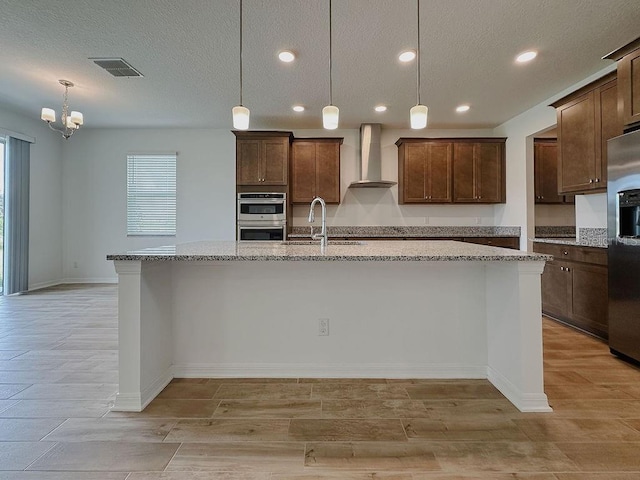 38120 Shale Stone Ct, Zephyrhills, FL 33540 - kitchen featuring wall chimney range hood, stainless steel appliances, light stone countertops, a spacious island, and decorative light fixtures