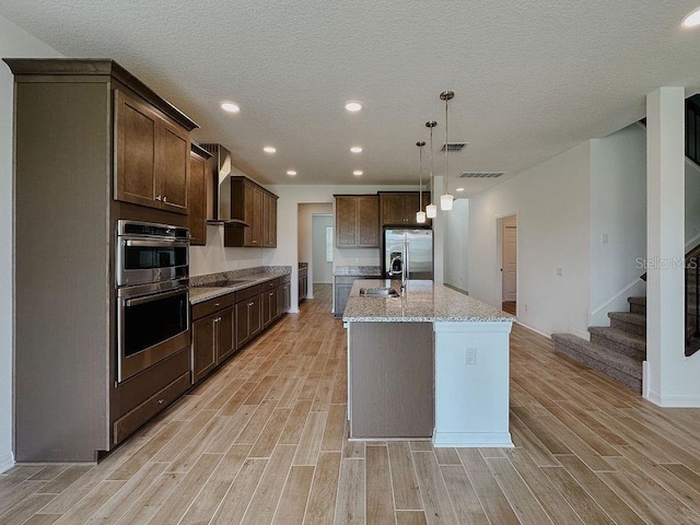 38120 Shale Stone Ct, Zephyrhills, FL 33540 - kitchen with stainless steel appliances, wall chimney exhaust hood, light wood-style flooring, dark brown cabinetry, and recessed lighting