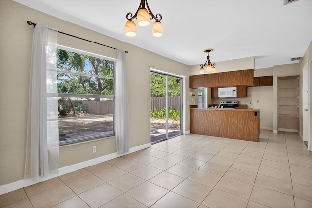 1600 Amberlea Dr N, Dunedin, FL 34698 - kitchen with white microwave, a chandelier, a peninsula, pendant lighting, and light tile patterned floors