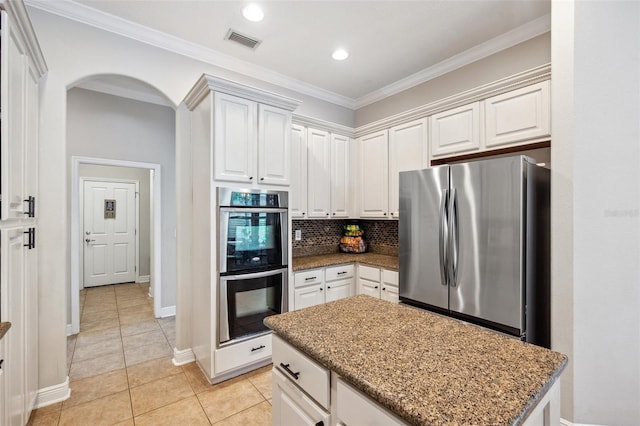 31646 Baymont Loop, Wesley Chapel, FL 33543 - kitchen featuring stainless steel appliances, decorative backsplash, light tile patterned floors, arched walkways, and dark stone countertops