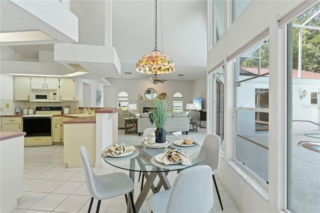 18561 Winding Oaks Blvd, Hudson, FL 34667 - dining area with ceiling fan, a high ceiling, light tile patterned floors, and a warm lit fireplace