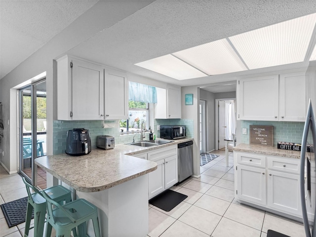 9109 134th Way, Seminole, FL 33776 - kitchen featuring stainless steel appliances, a peninsula, light countertops, light tile patterned floors, and white cabinetry