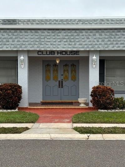 1102 Cara Dr, Largo, FL 33771 - doorway to property with mansard roof, a shingled roof, a porch, and stucco siding