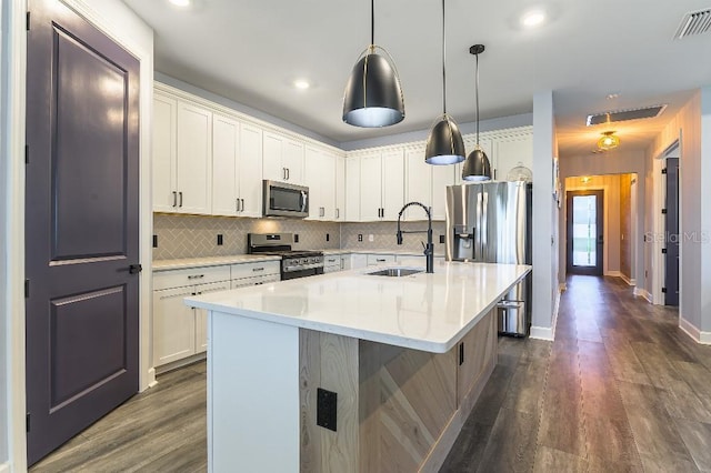 7683 Summerland Cv, Lakewood Ranch, FL 34202 - kitchen with stainless steel appliances, dark wood-style floors, decorative backsplash, light countertops, and a kitchen island with sink