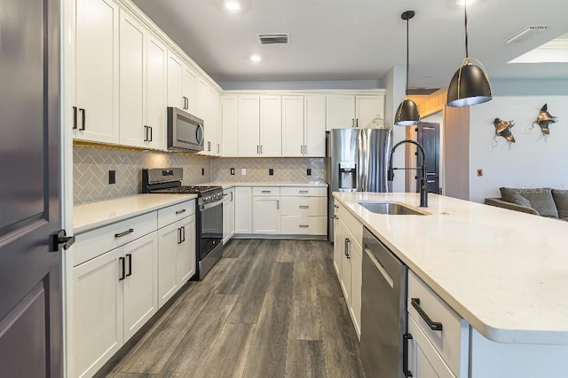 7683 Summerland Cv, Lakewood Ranch, FL 34202 - kitchen featuring appliances with stainless steel finishes, dark wood finished floors, an island with sink, tasteful backsplash, and decorative light fixtures