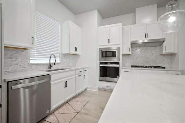2511 N Grady Ave Unit 43, Tampa, FL 33607 - kitchen featuring appliances with stainless steel finishes, under cabinet range hood, light wood-style flooring, white cabinets, and decorative backsplash