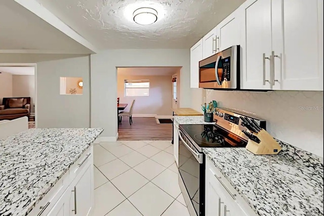 4505 S Clark Ave, Tampa, FL 33611 - kitchen featuring stainless steel microwave, electric range, light tile patterned floors, white cabinetry, and light stone counters