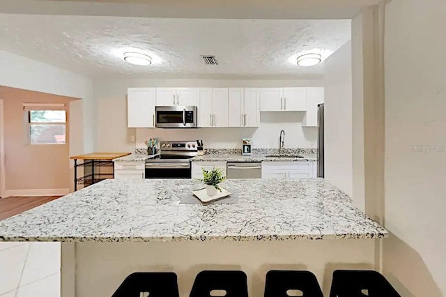 4505 S Clark Ave, Tampa, FL 33611 - kitchen with stainless steel appliances, a kitchen bar, white cabinetry, and light stone countertops