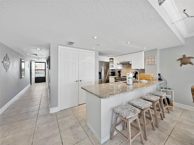 19440 Gulf Blvd Unit 301, Indian Rocks Beach, FL 33785 - kitchen featuring stainless steel fridge, a peninsula, a textured ceiling, under cabinet range hood, and light stone countertops