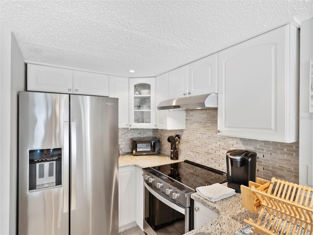 19440 Gulf Blvd Unit 301, Indian Rocks Beach, FL 33785 - kitchen featuring appliances with stainless steel finishes, under cabinet range hood, light stone counters, backsplash, and white cabinetry