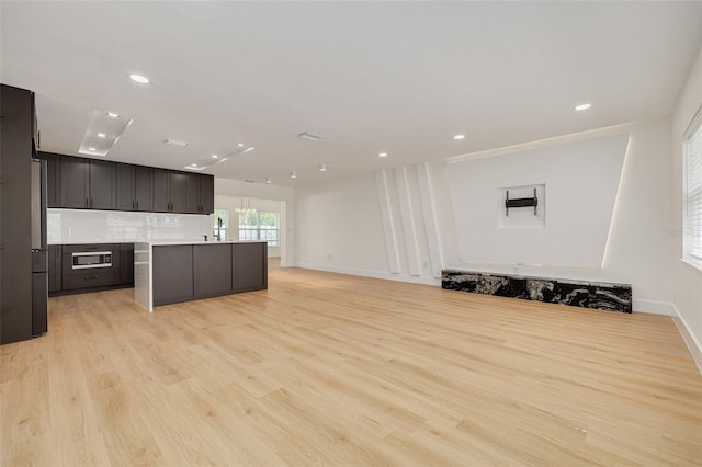 1723 Cypress Ave, Belleair, FL 33756 - kitchen featuring light wood-style floors, open floor plan, tasteful backsplash, light countertops, and an island with sink