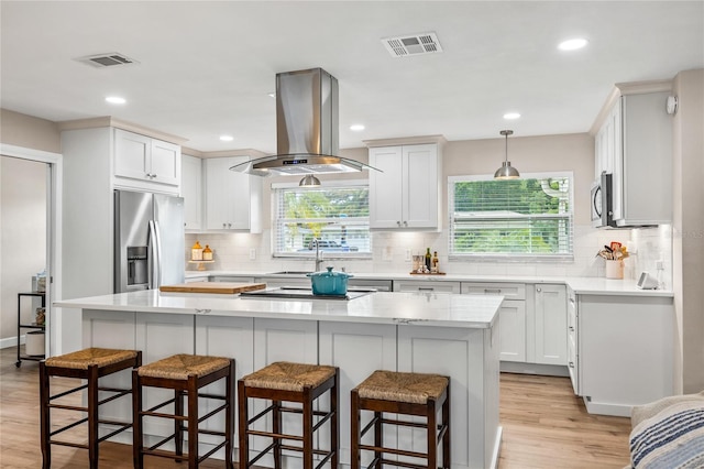 1251 Fairway Dr, Dunedin, FL 34698 - kitchen featuring island range hood, stainless steel appliances, light wood-style floors, light countertops, and backsplash