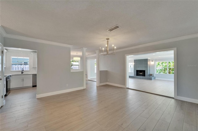 4518 Helena St NE, Saint Petersburg, FL 33703 - unfurnished living room featuring a chandelier, a textured ceiling, light wood-style flooring, ornamental molding, and a fireplace