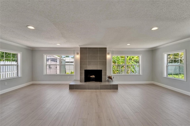 4518 Helena St NE, Saint Petersburg, FL 33703 - unfurnished living room with ornamental molding, a textured ceiling, a tile fireplace, plenty of natural light, and wood finished floors