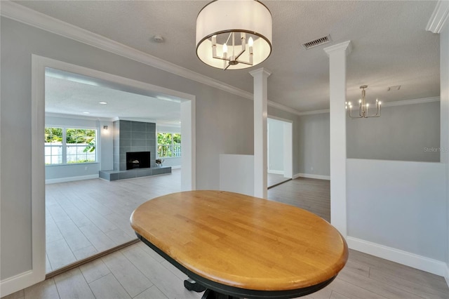 4518 Helena St NE, Saint Petersburg, FL 33703 - dining room featuring a chandelier, decorative columns, light wood finished floors, ornamental molding, and a tile fireplace