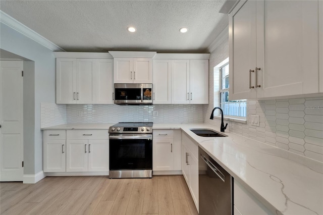 4518 Helena St NE, Saint Petersburg, FL 33703 - kitchen featuring appliances with stainless steel finishes, crown molding, light wood-style flooring, a textured ceiling, and white cabinetry