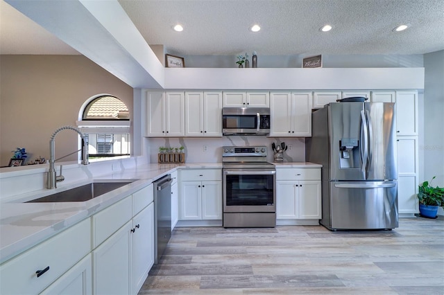 3704 Darston St, Palm Harbor, FL 34685 - kitchen with appliances with stainless steel finishes, white cabinets, light wood-style floors, light stone countertops, and a textured ceiling