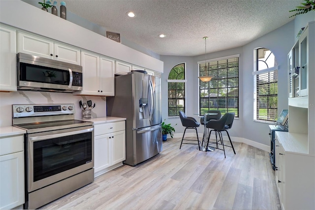 3704 Darston St, Palm Harbor, FL 34685 - kitchen with appliances with stainless steel finishes, a textured ceiling, light countertops, white cabinets, and light wood-style flooring