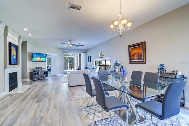 3704 Darston St, Palm Harbor, FL 34685 - dining space with a chandelier, light wood-type flooring, a tile fireplace, a textured ceiling, and a ceiling fan