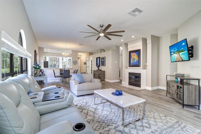 3704 Darston St, Palm Harbor, FL 34685 - living room with a chandelier, light wood-style floors, a ceiling fan, a tile fireplace, and a textured ceiling