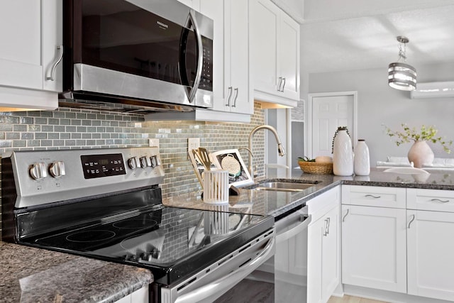 4300 Maple St NE, Saint Petersburg, FL 33703 - kitchen with stainless steel appliances, white cabinetry, dark stone counters, backsplash, and decorative light fixtures