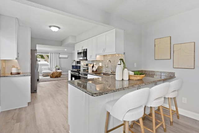4300 Maple St NE, Saint Petersburg, FL 33703 - kitchen with stainless steel appliances, dark stone countertops, light wood-type flooring, decorative backsplash, and a kitchen bar