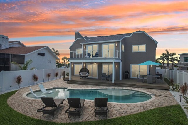 311 22nd St, Belleair Beach, FL 33786 - back of property at dusk featuring a balcony, a fenced backyard, a patio, and stucco siding