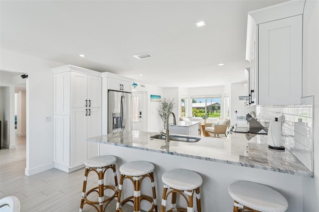 311 22nd St, Belleair Beach, FL 33786 - kitchen with stainless steel fridge, a peninsula, light stone counters, white cabinets, and tasteful backsplash