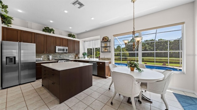 12439 Bristol Commons Cir, Tampa, FL 33626 - kitchen featuring appliances with stainless steel finishes, a chandelier, light countertops, backsplash, and a center island