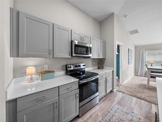 13105 Fruitville Way, Riverview, FL 33579 - kitchen with stainless steel appliances, gray cabinetry, light countertops, lofted ceiling, and light wood-style flooring