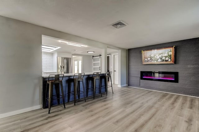 7031 Magnolia Valley Dr, New Port Richey, FL 34653 - kitchen with stainless steel fridge with ice dispenser, a breakfast bar area, light wood finished floors, a glass covered fireplace, and open floor plan
