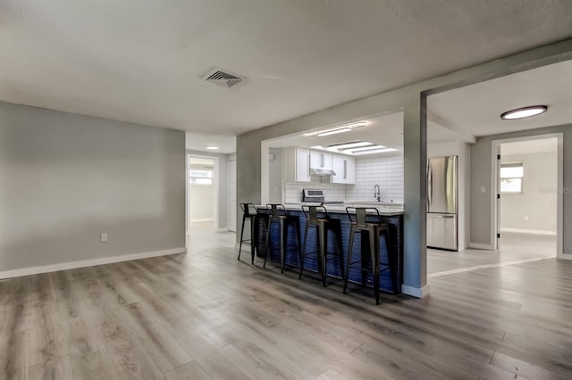 7031 Magnolia Valley Dr, New Port Richey, FL 34653 - kitchen featuring freestanding refrigerator, range, light wood-style flooring, a breakfast bar area, and white cabinetry