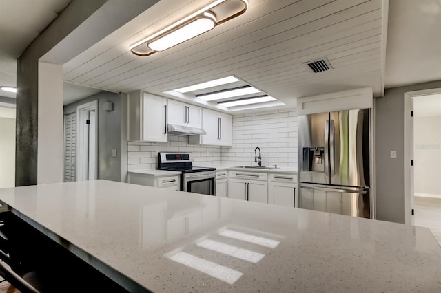 7031 Magnolia Valley Dr, New Port Richey, FL 34653 - kitchen with appliances with stainless steel finishes, under cabinet range hood, backsplash, white cabinets, and light stone countertops