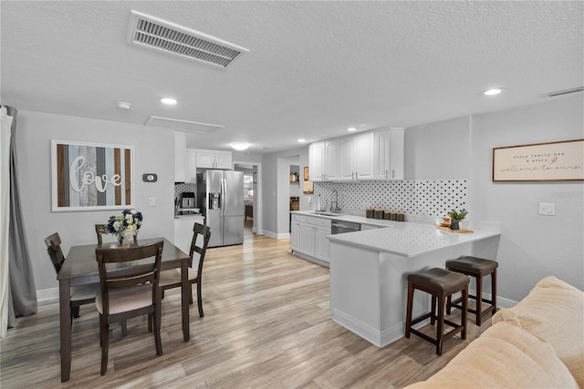 4460 67th St N, Saint Petersburg, FL 33709 - kitchen featuring appliances with stainless steel finishes, a peninsula, a textured ceiling, a kitchen breakfast bar, and decorative backsplash