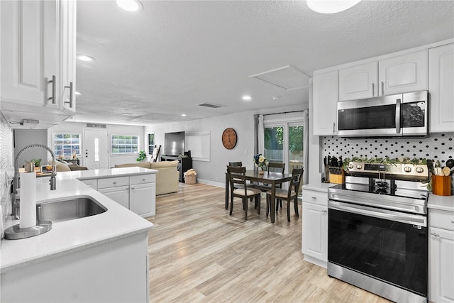 4460 67th St N, Saint Petersburg, FL 33709 - kitchen featuring appliances with stainless steel finishes, open floor plan, white cabinetry, light countertops, and light wood-type flooring