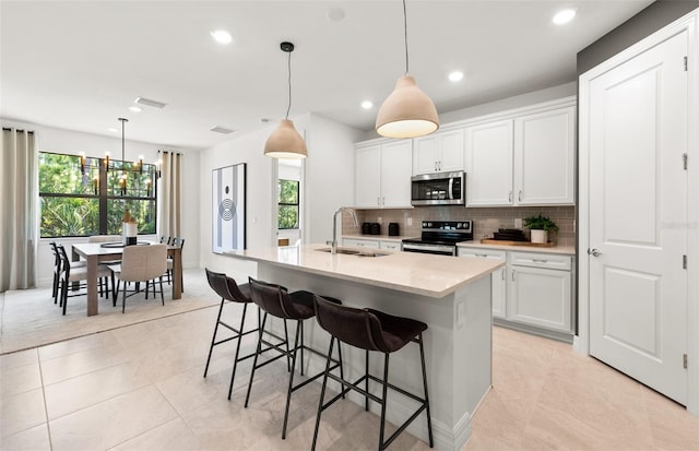 5719 Silverside Pine Ct, Lakewood Ranch, FL 34211 - kitchen featuring stainless steel appliances, decorative backsplash, a kitchen bar, white cabinetry, and a center island with sink