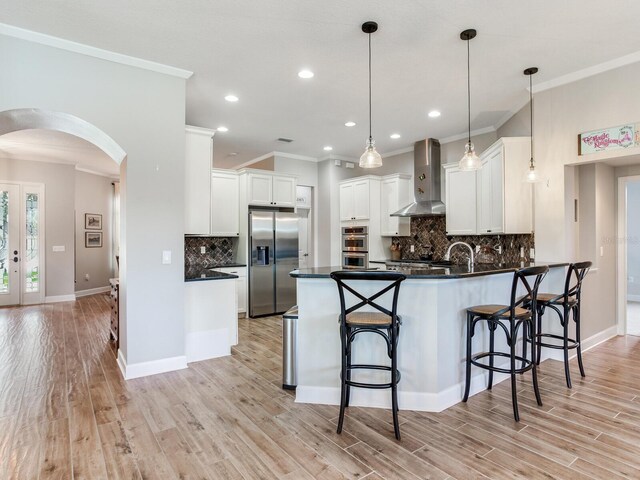 3503 Graycliff Ln, Brandon, FL 33511 - kitchen featuring stainless steel appliances, wall chimney range hood, a peninsula, arched walkways, and light wood-style floors