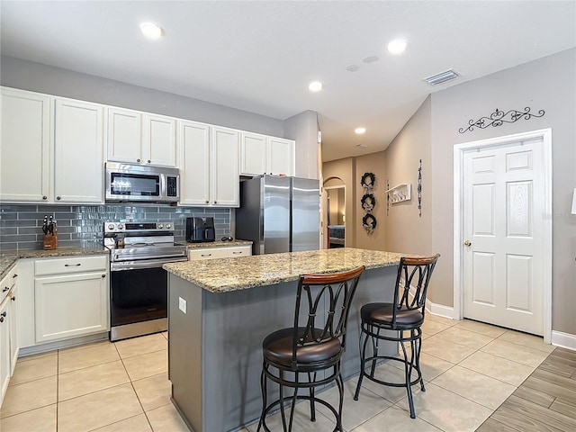 18339 Fish Loop, Land O Lakes, FL 34638 - kitchen with appliances with stainless steel finishes, a kitchen island, backsplash, light stone counters, and a kitchen breakfast bar