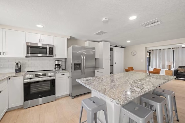 201 S St, Palm Harbor, FL 34683 - kitchen with appliances with stainless steel finishes, a barn door, a breakfast bar area, white cabinetry, and light wood-type flooring